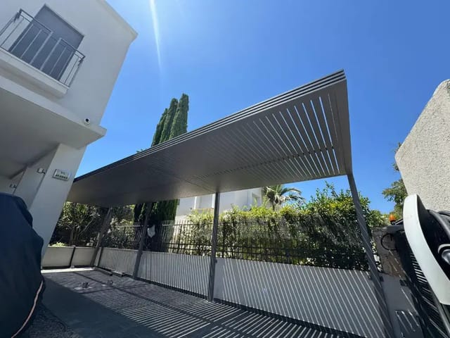 פרגולה לחניה בגוון אפור על עמודים דקים, במבט מלמטה מול שמיים כחולים