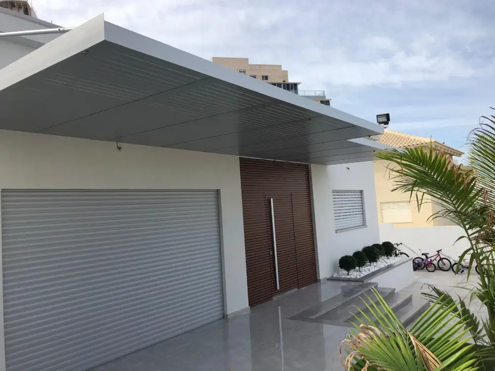 פרגולה תלויה אפורה בהירה עם קירוי אטום מעל דלת הכניסה ודלת החניה