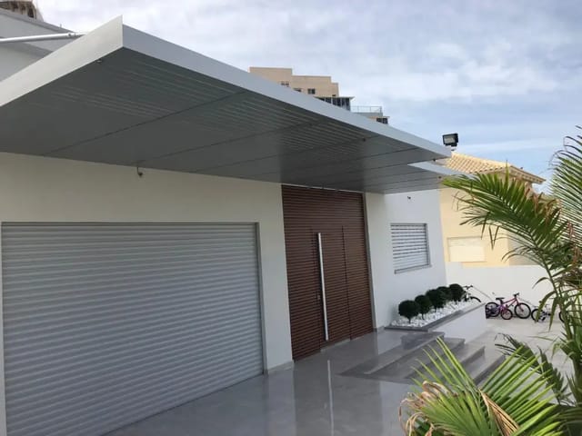 פרגולה תלויה אפורה בהירה עם קירוי אטום מעל דלת הכניסה ודלת החניה