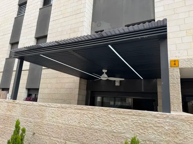 פרגולת אלומיניום אנתרציט על עמודים עם פסי תאורה ומאוורר בכניסה לדירת גן