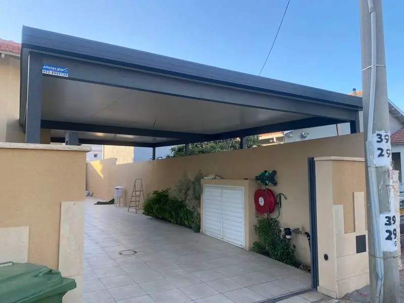 קירוי אלומיניום אפור כהה על עמודים מעל שביל כניסה מרוצף בחצר בית