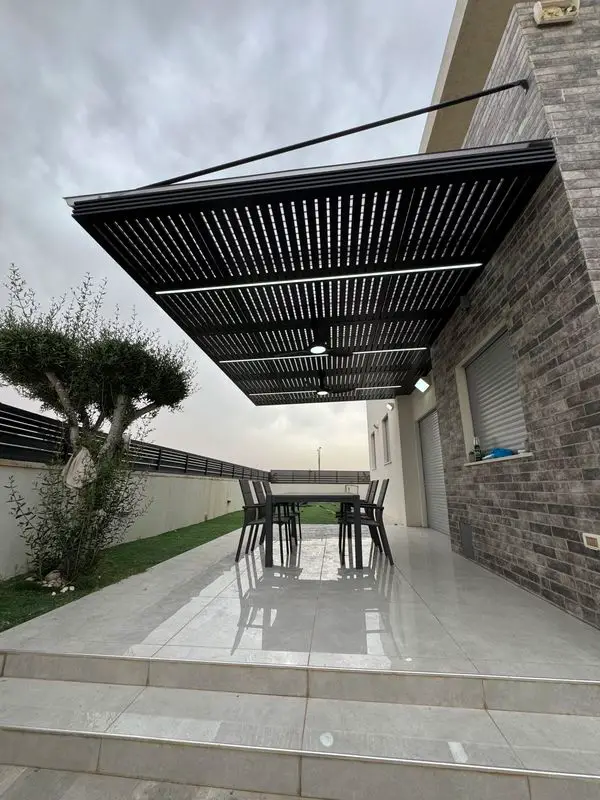 פרגולת אלומיניום תלויה שחורה עם מוט תלייה ותאורה מעל פינת אוכל בפטיו