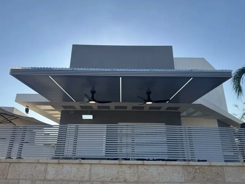 פרגולת אלומיניום אפורה עם פסי תאורה ושני מאווררי תקרה מעל מרפסת הבית