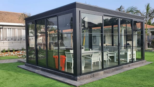 מבנה אלומיניום שחור סגור בזכוכית עם פינת אוכל, עומד חופשי על דשא