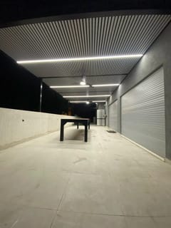 פרגולה עם תקרת שלבים ופסי לד בלילה לצד תריסי גלילה – דגם לוקס פארקינג