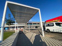 פרגולה לבנה עם שלבים על עמודים מעל שביל מרוצף באתר מסחרי