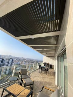 פרגולה תלויה עם שלבים כהים במרפסת מגדל עם פינת ישיבה ואוכל