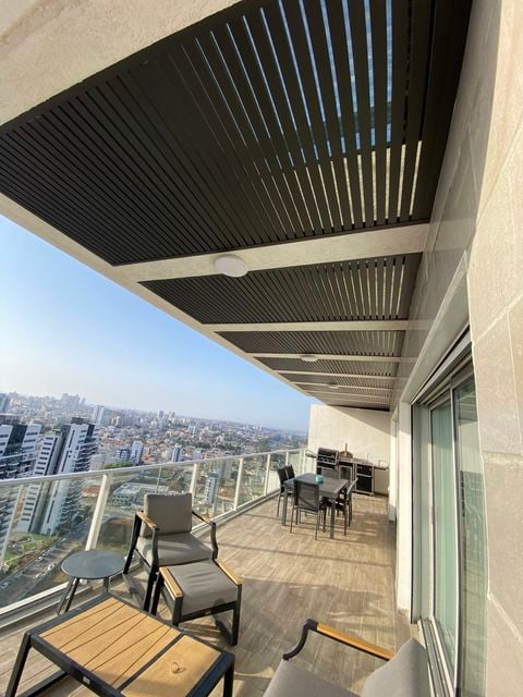 פרגולה תלויה עם שלבים כהים במרפסת מגדל עם פינת ישיבה ואוכל