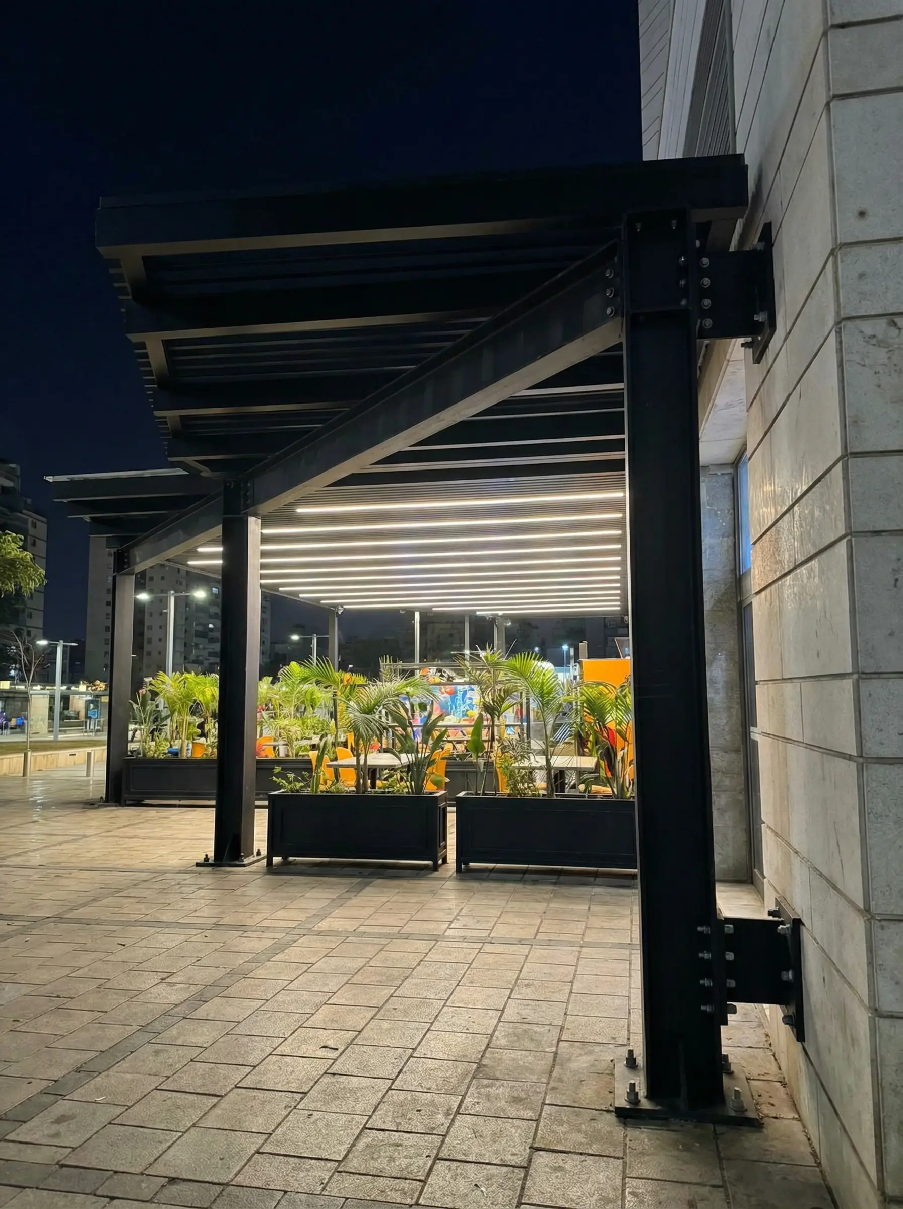 עמוד פרגולה שחור מחובר בברגים לקיר אבן, מבט אל תוך הפרגולה בלילה
