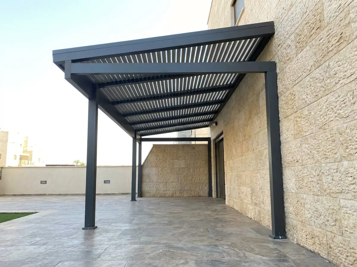 פרגולה אנתרציט צמודה לקיר אבן עם רפפות ועמודים ברחבה מרוצפת