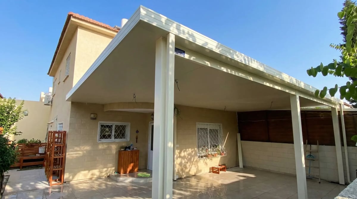 פרגולה מקורה לבנה בפינת בית דו-קומתי, מבט מהצד באור שמש