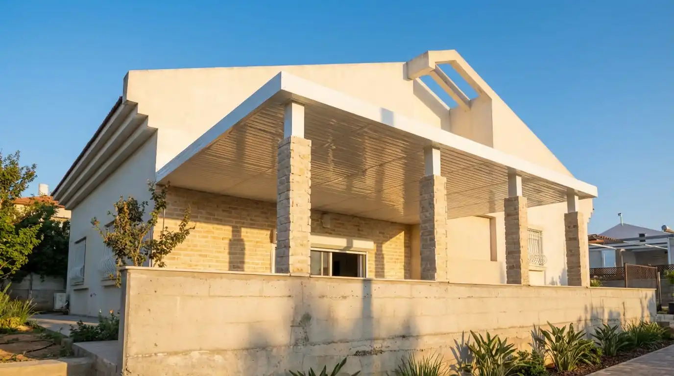 פרגולה לבנה על עמודים מחופי אבן לאורך מרפסת בית פרטי, מבט מהגינה