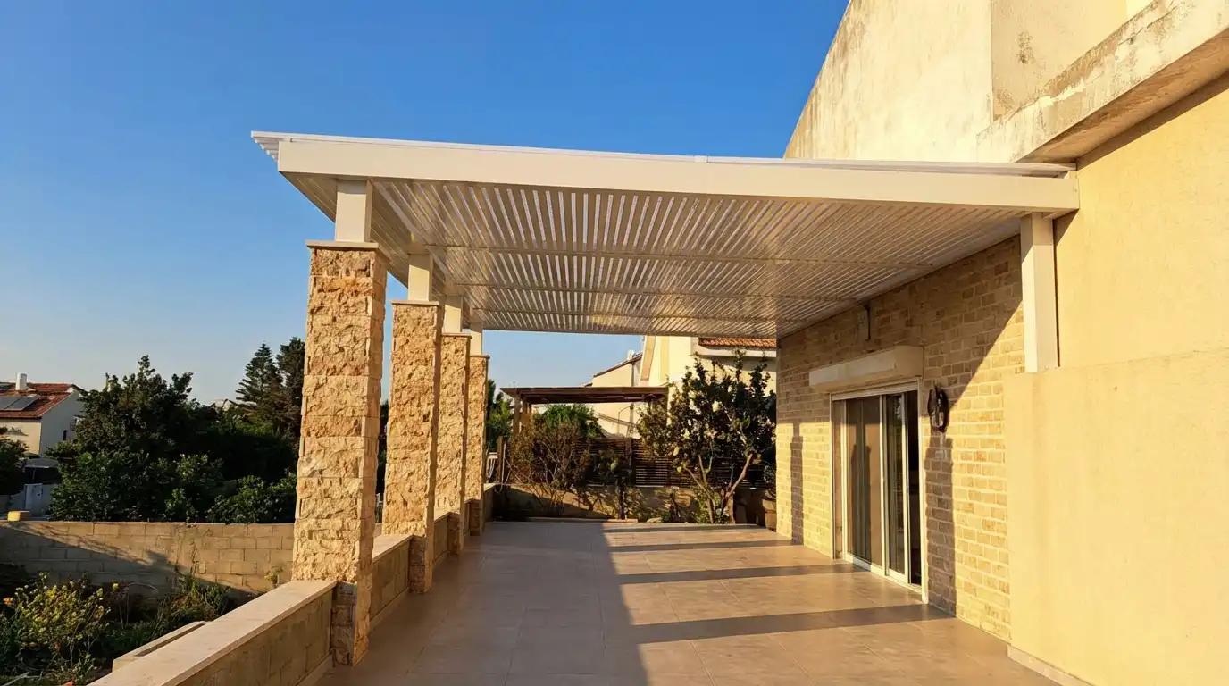 פרגולה לבנה לאורך מרפסת מרוצפת ארוכה, על עמודים מחופי אבן