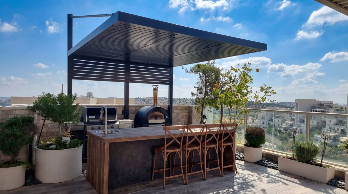 מטבח חוץ עם גריל, תנור פיצה ובר כיסאות תחת פרגולה אפורה על הגג